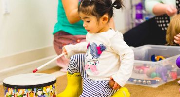 Montessori Program Toddler Playing A Drum While Holding A Ball