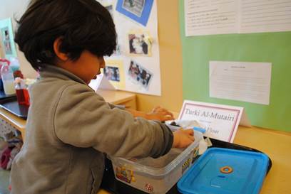 A little boy reaching his hands out to touch a science fair project in a plastic container.