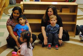 Two mothers sitting with their son’s in their lap and a little girl listening to someone speaking.