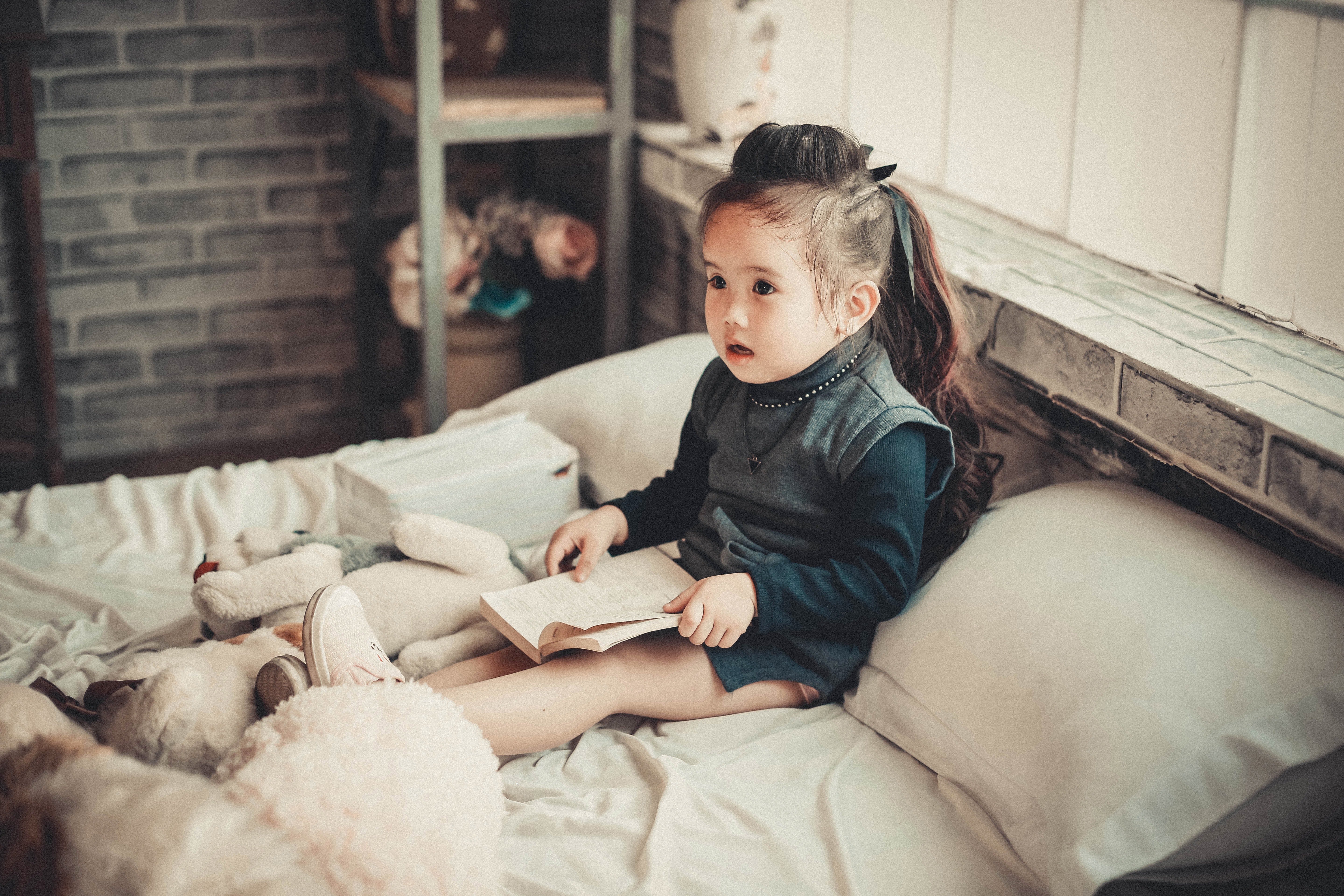 A little girl sitting upright in bed reading like an adult.
